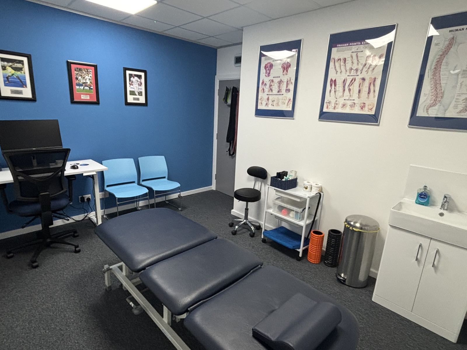 A private treatment room with a treatment couch and anatomy posters