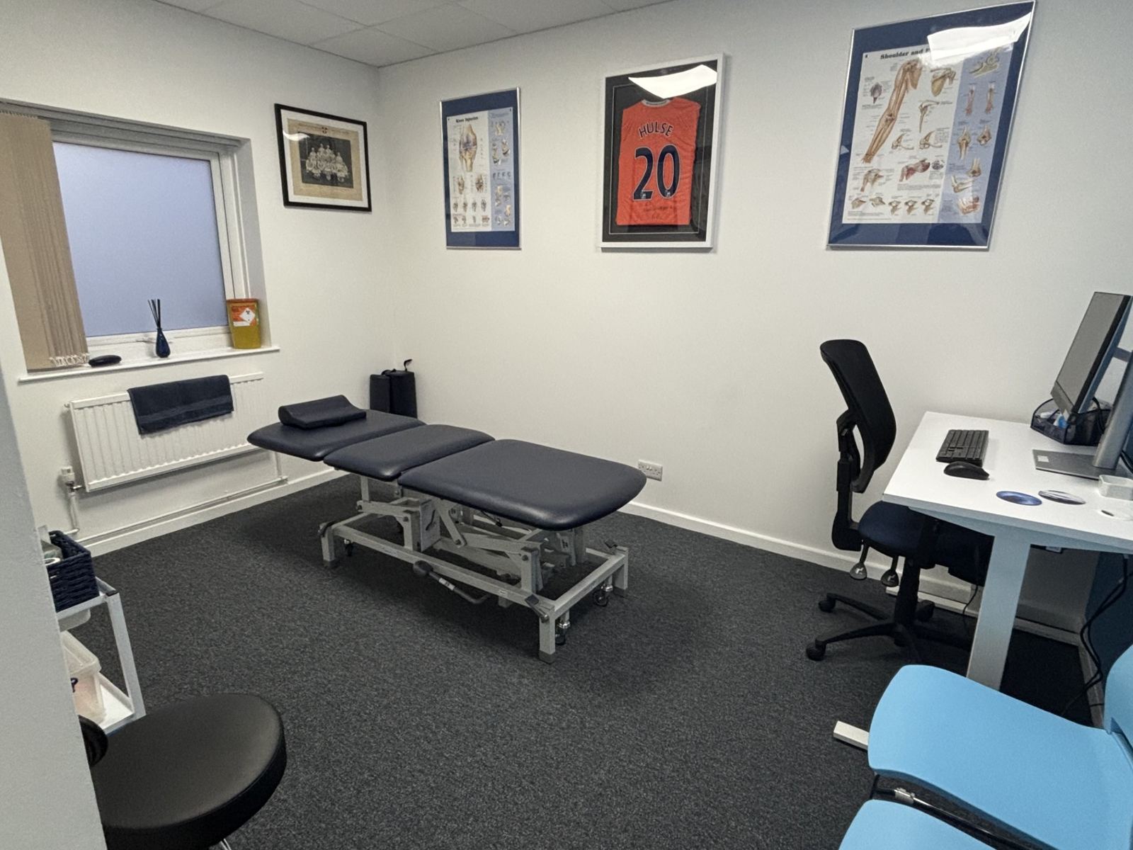 A private treatment room with an adjustable couch, desk and framed cricket shirt