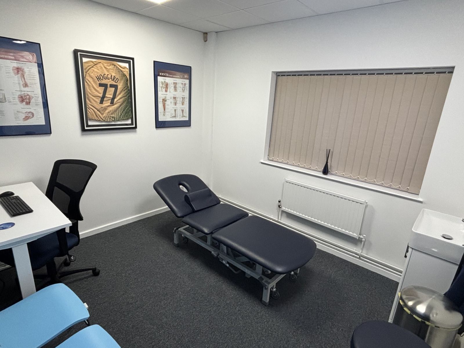 A second treatment room with a couch, anatomy posters and a framed football shirt