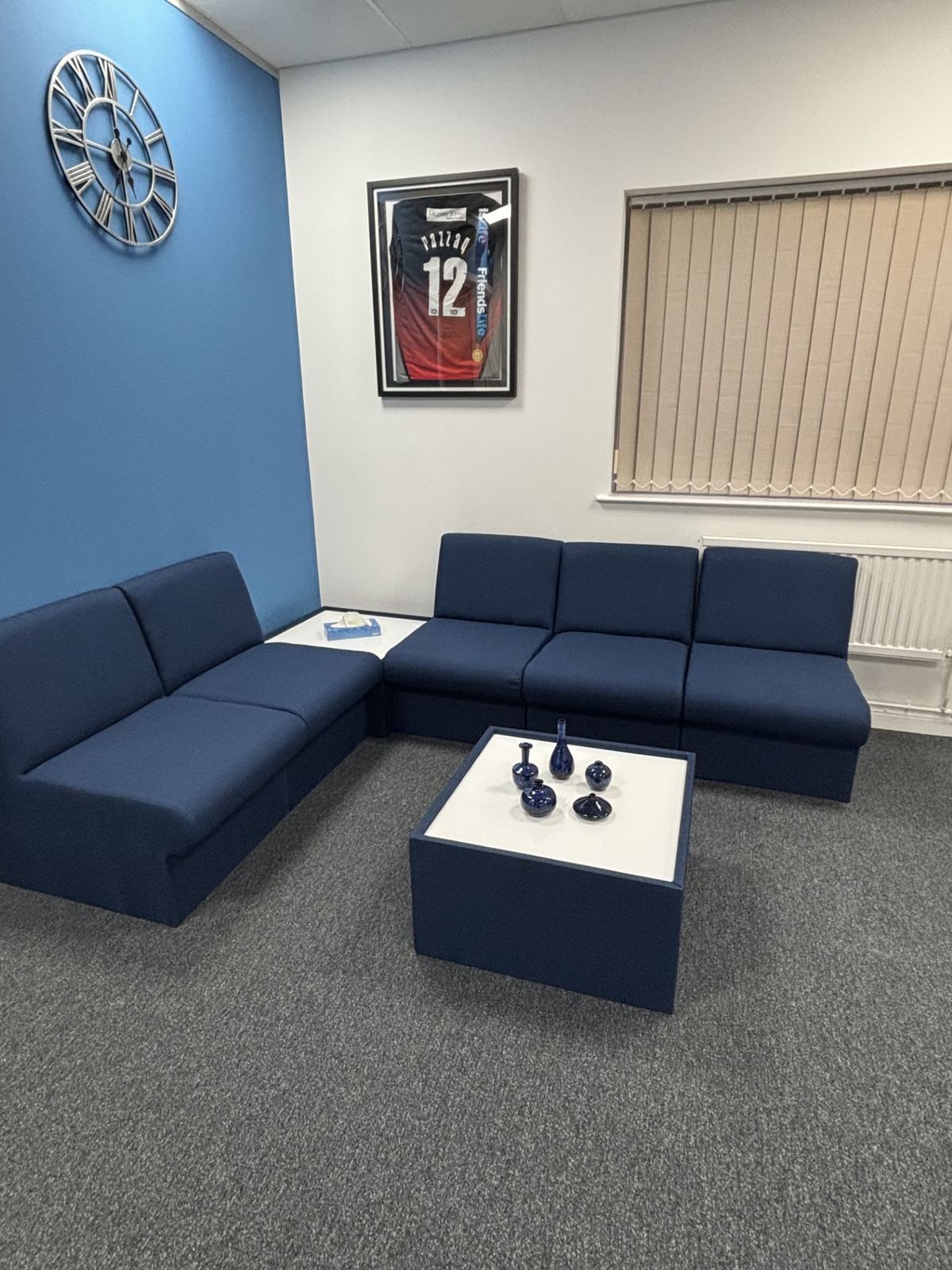 The clinic waiting area with navy sofas and a framed signed sports shirt on the wall