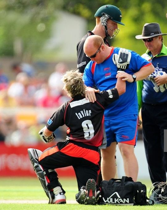 Physio attending to a batsman on the field during a professional cricket match
