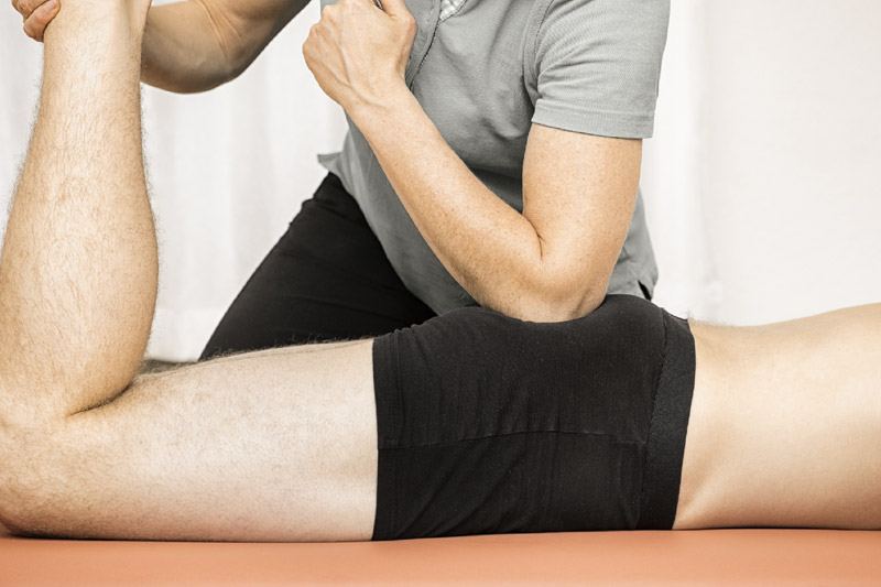 Therapist leaning in to massage a client's lower back and hip