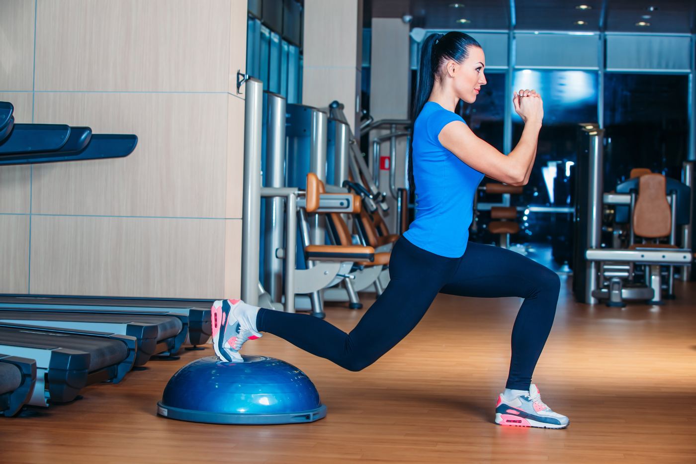 Woman doing a split squat with her back foot on a balance trainer in a gym
