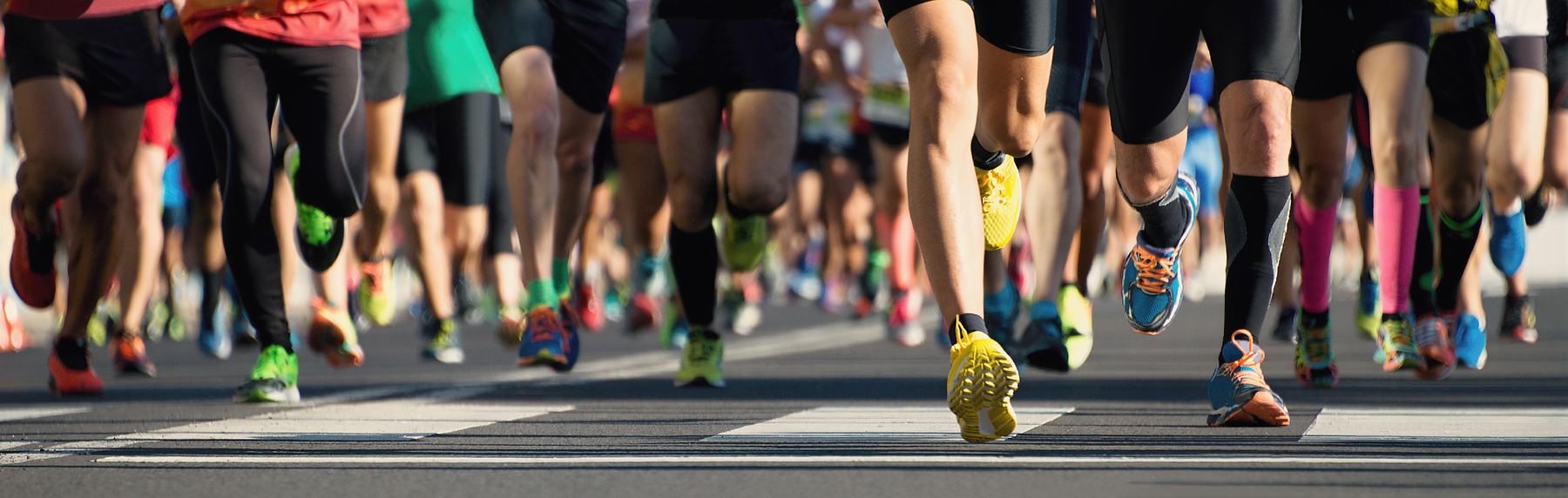 A large group of runners in a road race, seen from the knees down