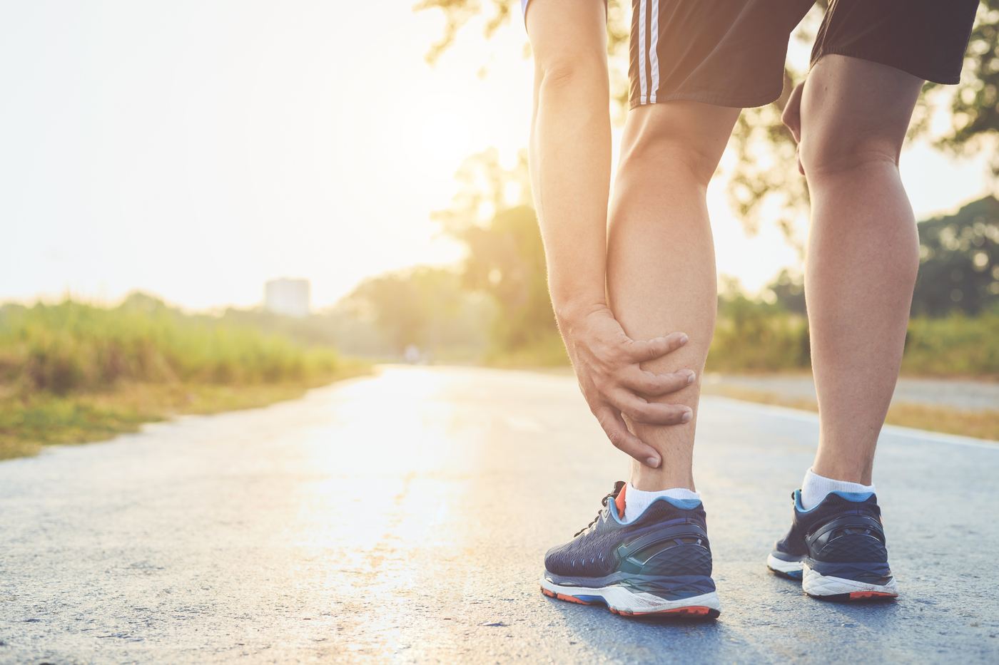 Runner on a sunny road stopping to hold the back of his lower leg